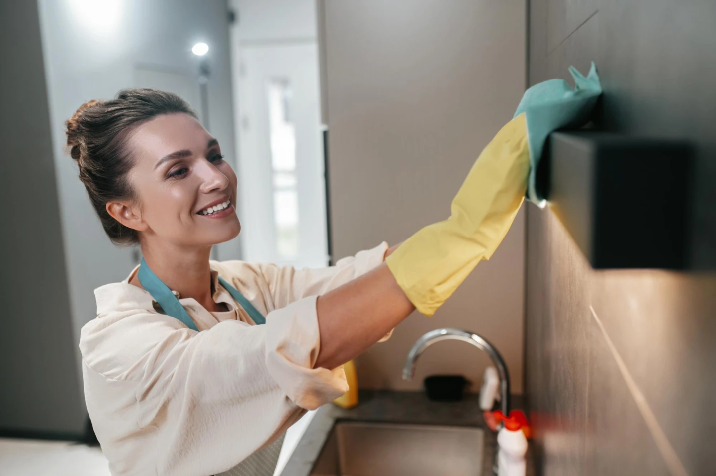 Employée de maison souriante nettoyant un meuble de cuisine avec des gants jaunes